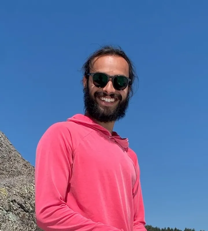 A photo of CJ in a pink shirt and sunglasses smiling at the camera.
